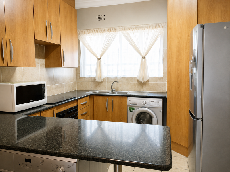 A functional kitchen featuring wood-finish cabinetry, granite countertops, a double sink, and integrated laundry appliances, offering a practical layout for daily use.