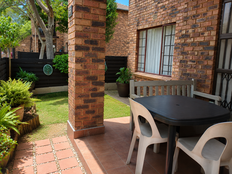 A private outdoor patio area featuring tiled flooring, a brick pillar, and direct access to a small garden space.