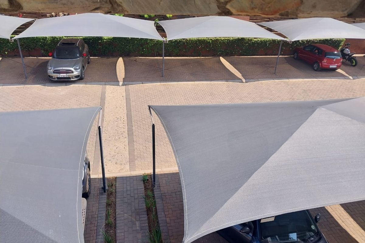 Elevated view of the apartment complex parking area featuring paved surfaces and multiple shade-cloth carports.