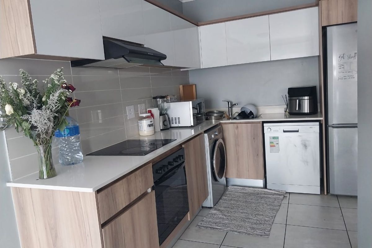 Modern kitchen featuring two-tone cabinetry, stone countertops, integrated oven, hob, extractor fan, and dedicated space for laundry and dishwasher appliances.