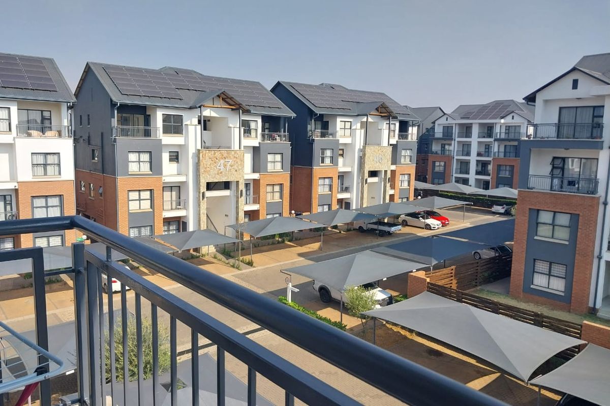 Elevated view of a modern apartment complex featuring brick and plaster facades, solar panels, and covered parking bays.