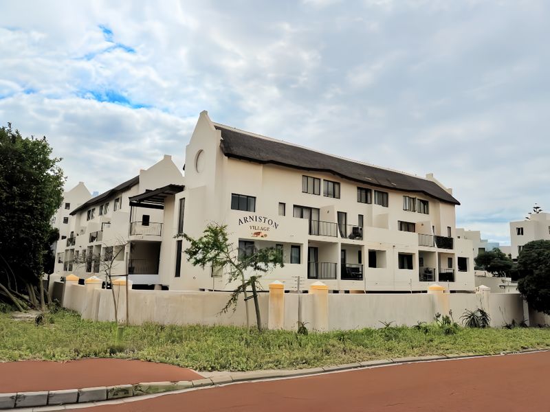 Exterior view of the Arniston Village apartment complex featuring traditional thatched roofing, multiple balconies, and a secure perimeter wall.