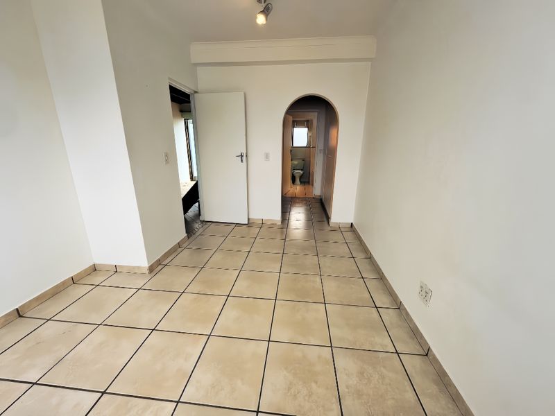 A clean, empty hallway featuring neutral tiled flooring and an arched entryway leading to an adjacent room.