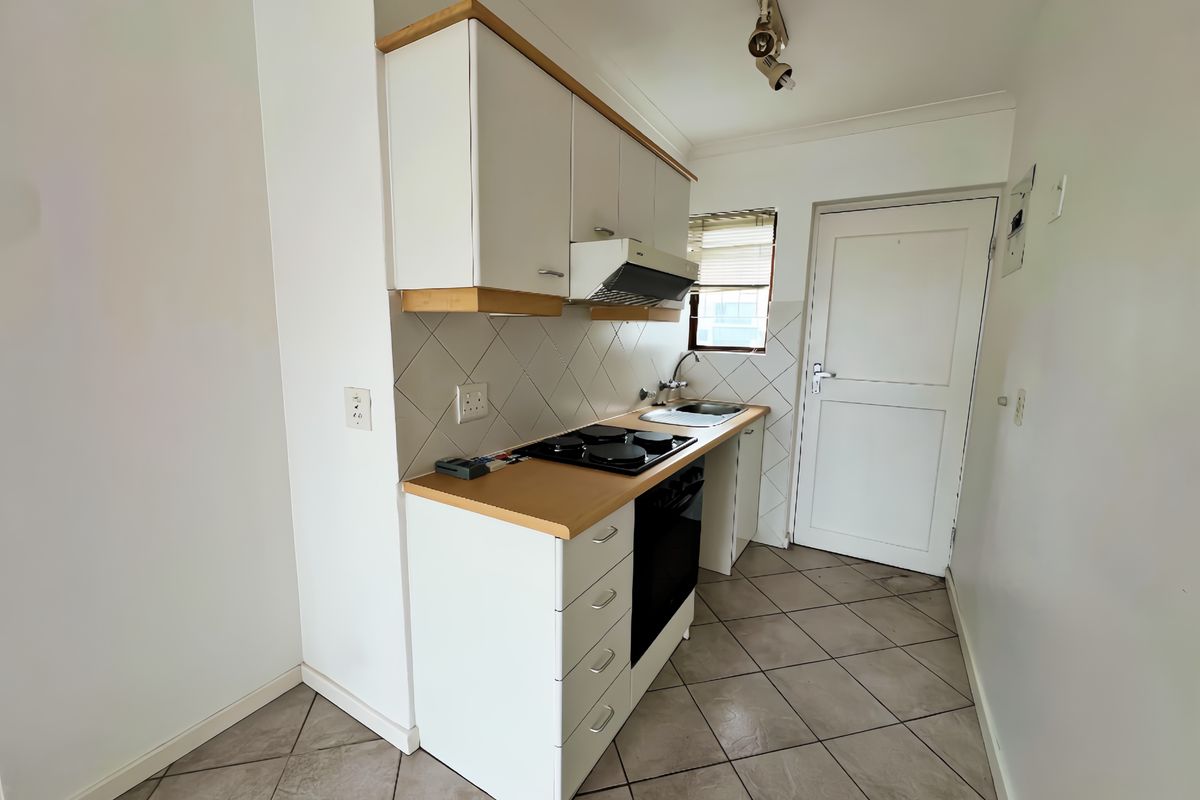 A compact, functional kitchen featuring white cabinetry, a laminate countertop, built-in oven and hob, and tiled flooring.