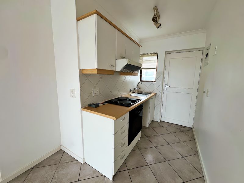 A compact, functional kitchen featuring white cabinetry, a laminate countertop, built-in oven and hob, and tiled flooring.