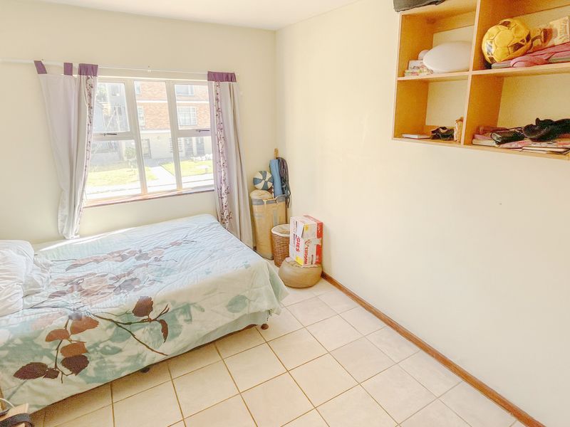 A functional bedroom featuring tiled flooring, built-in wall shelving, and a window providing natural light.