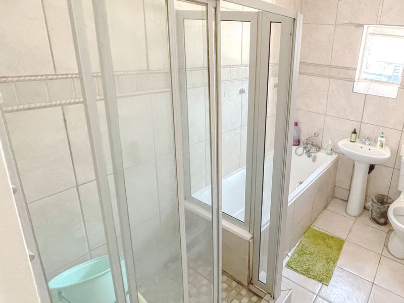 A functional bathroom featuring a shower enclosure, bathtub, pedestal basin, and toilet with neutral wall and floor tiling.