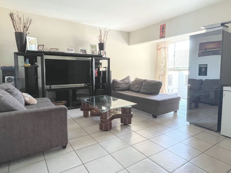 A spacious living room featuring neutral tiled flooring and natural light from a large window, offering a versatile layout for comfortable seating arrangements.