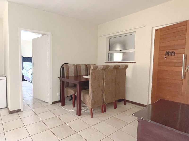 A functional dining area featuring tiled flooring, a horizontal sliding window, and a solid timber door leading to an adjacent bedroom.