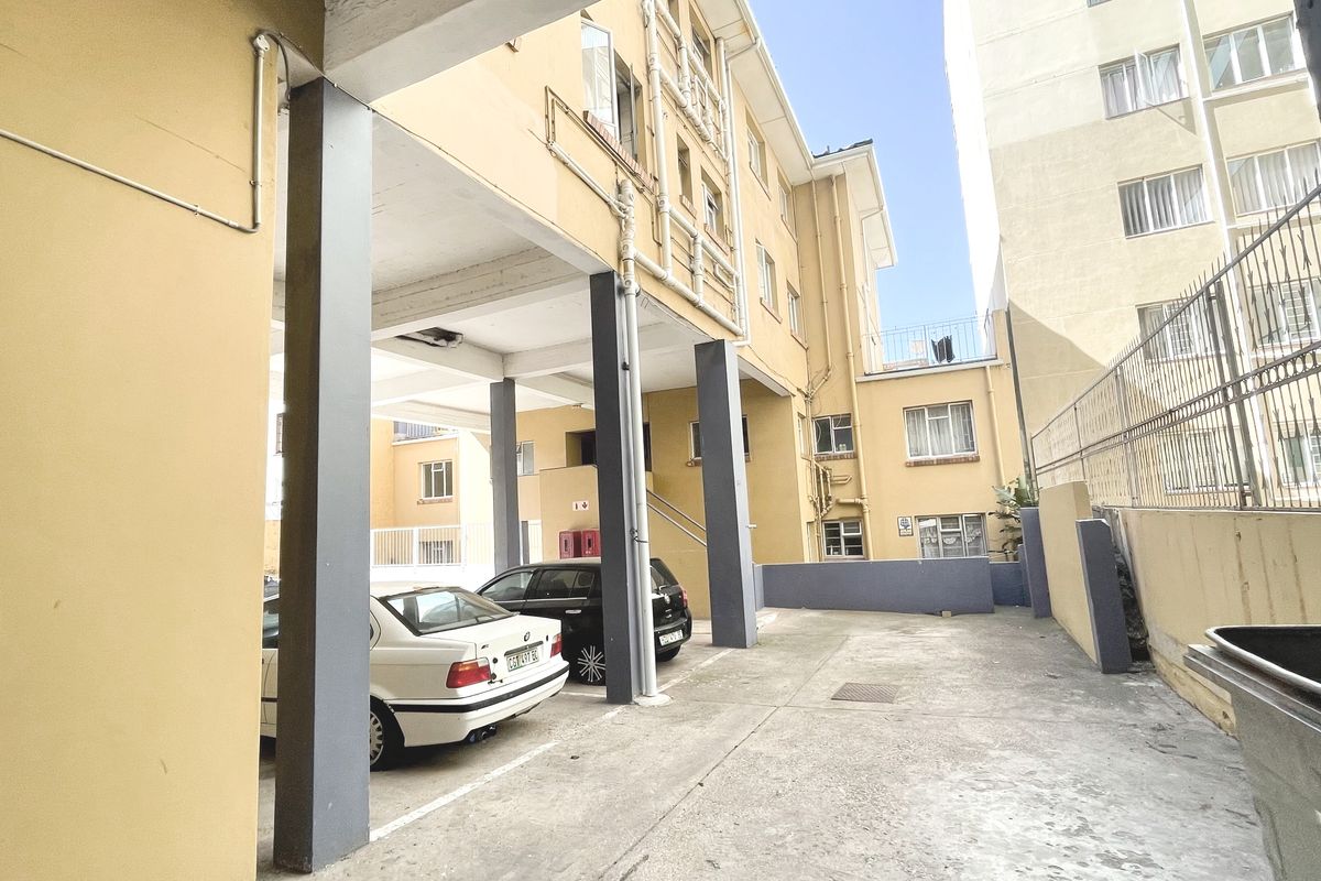 Rear exterior view of the apartment building showing covered parking area, concrete columns, and paved ground surface.