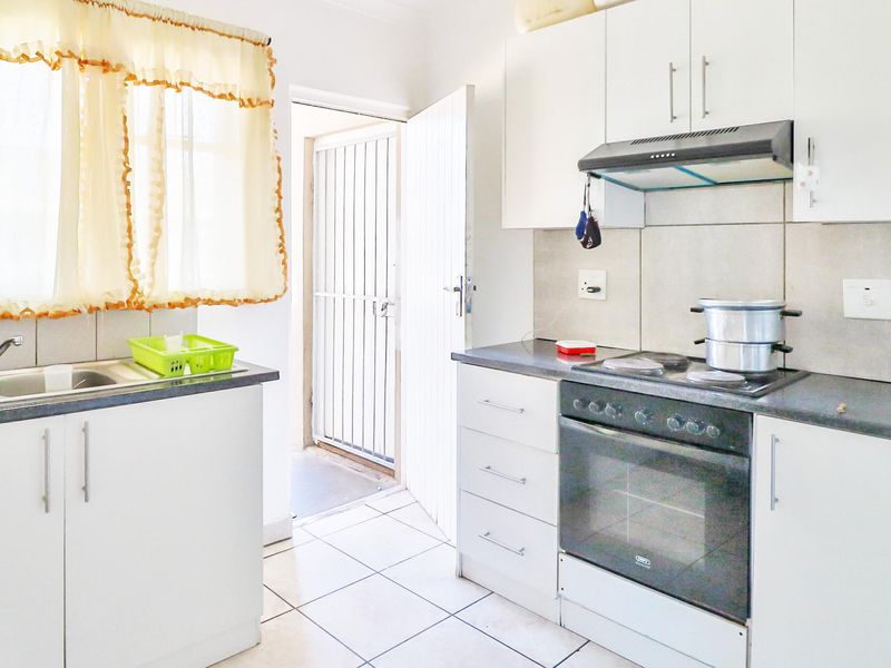 A functional kitchen featuring white cabinetry, a built-in oven and stove, tiled flooring, and direct access to an exterior security gate.