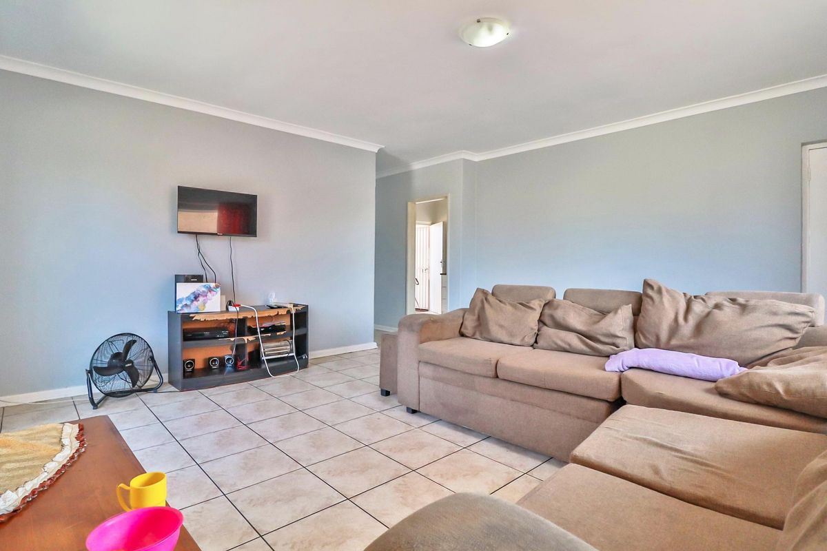 A spacious living room featuring neutral wall tones, tiled flooring, and coved ceiling cornices, providing a functional and well-lit area for relaxation.