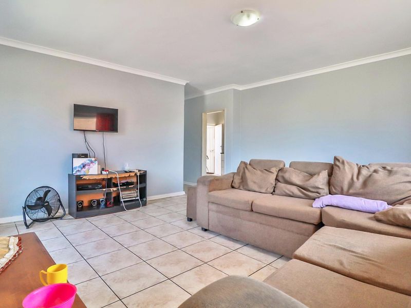 A spacious living room featuring neutral wall tones, tiled flooring, and coved ceiling cornices, providing a functional and well-lit area for relaxation.