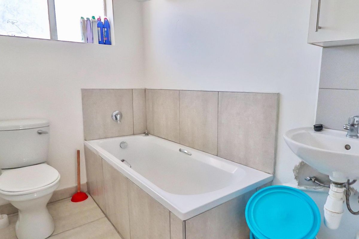 A functional bathroom featuring a bathtub with tiled surround, a pedestal basin, and a standard toilet.