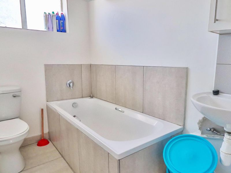 A functional bathroom featuring a bathtub with tiled surround, a pedestal basin, and a standard toilet.