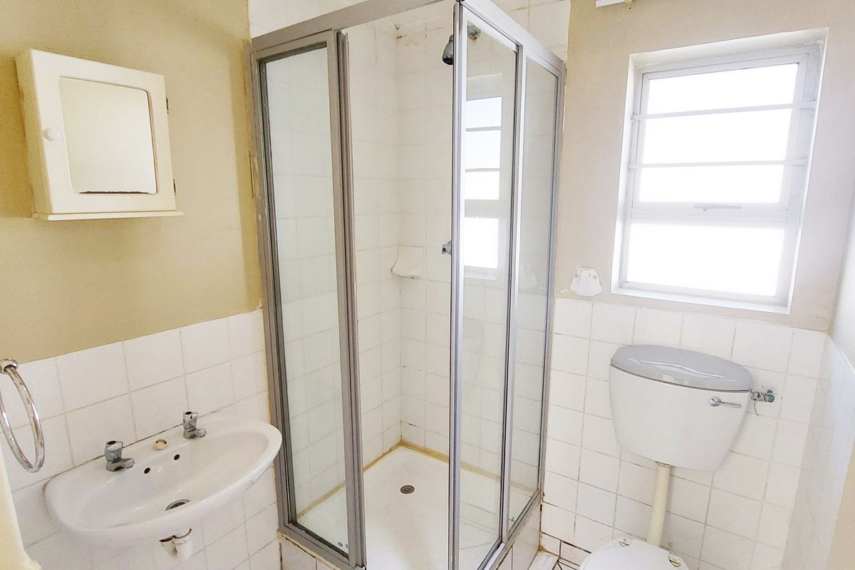 A functional bathroom featuring a shower enclosure, pedestal basin, and toilet, with tiled finishes throughout. The space is ready for modernization.