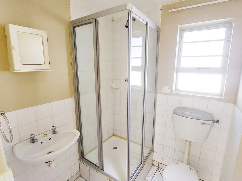 A functional bathroom featuring a shower enclosure, pedestal basin, and toilet, with tiled finishes throughout. The space is ready for modernization.