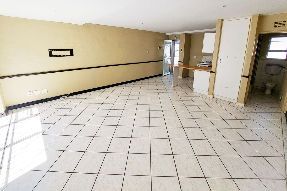 An open-plan living and kitchen area featuring tiled flooring, a breakfast bar, and built-in storage, offering a blank canvas for renovation.