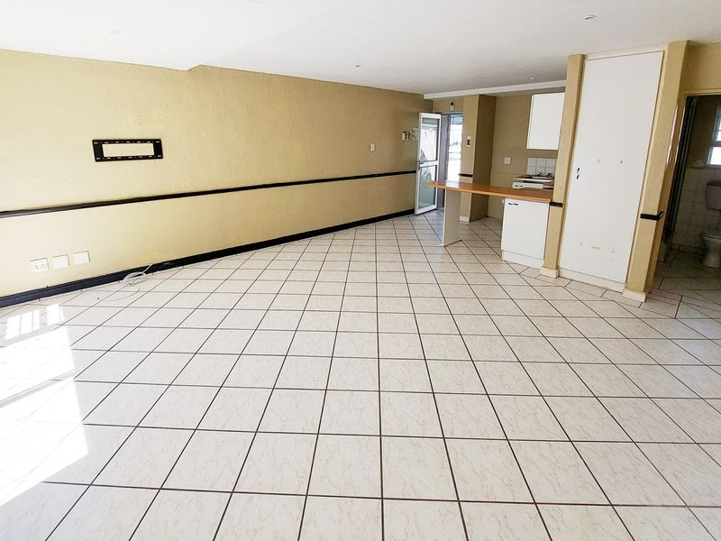 An open-plan living and kitchen area featuring tiled flooring, a breakfast bar, and built-in storage, offering a blank canvas for renovation.