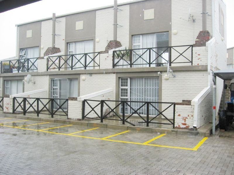 Exterior view of a multi-level apartment complex featuring brick facades, private balconies with metal railings, and dedicated paved parking spaces.