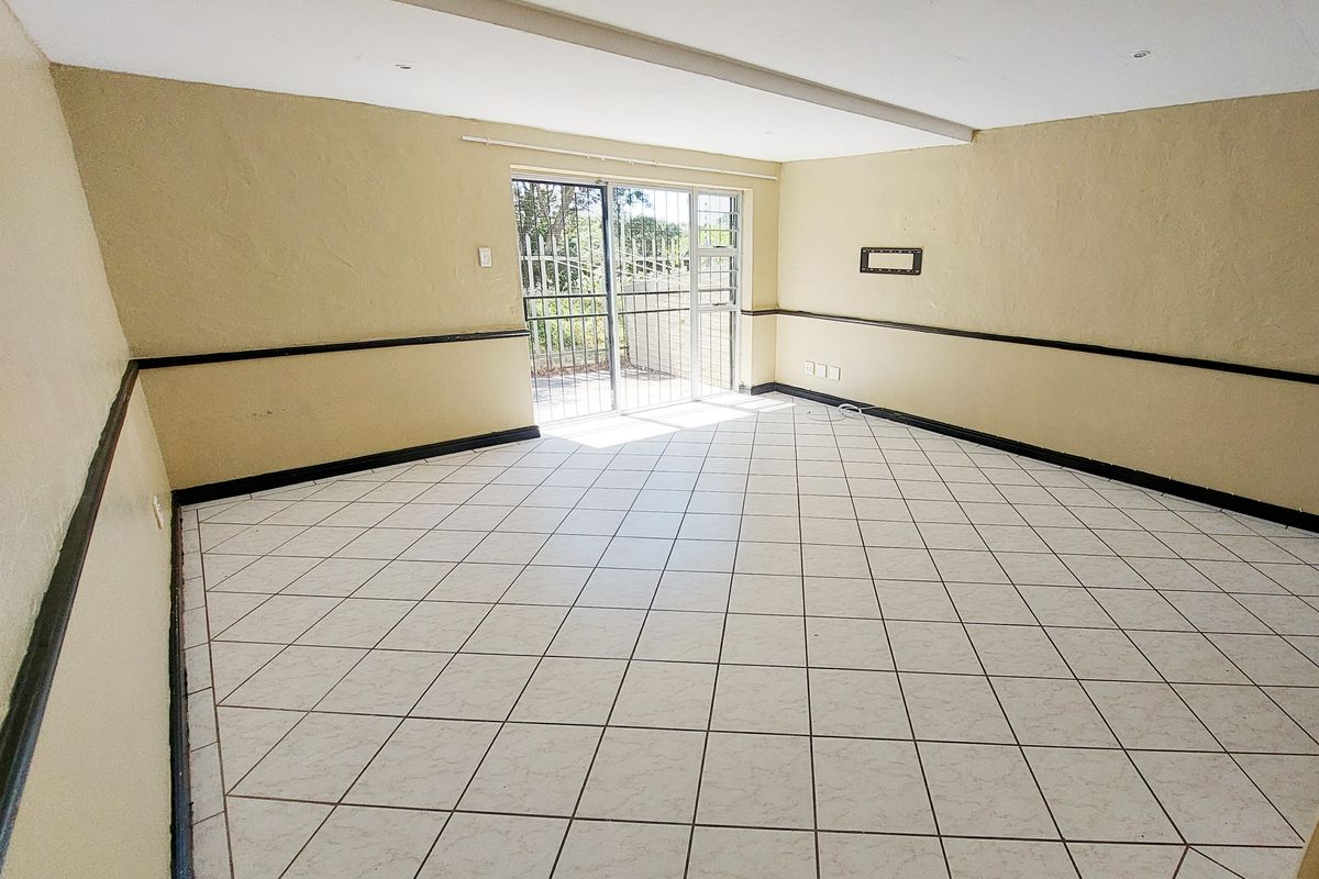 An empty living room featuring tiled flooring, a sliding glass door with security gate, and decorative chair rail molding.