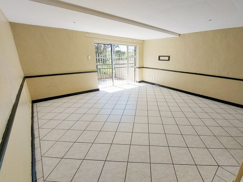 An empty living room featuring tiled flooring, a sliding glass door with security gate, and decorative chair rail molding.