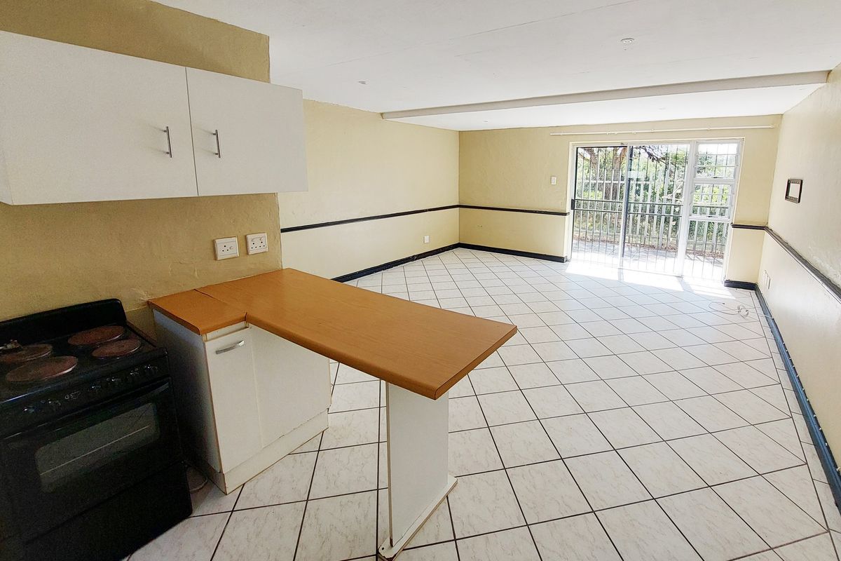 Spacious open-plan living and kitchen area featuring tiled flooring, built-in cabinetry, an electric stove, and direct access to an outdoor space via a security gate.