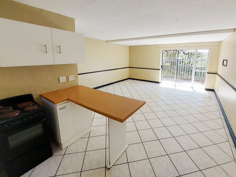 Spacious open-plan living and kitchen area featuring tiled flooring, built-in cabinetry, an electric stove, and direct access to an outdoor space via a security gate.