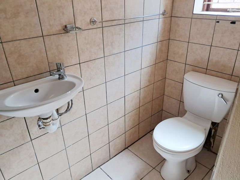 A compact guest bathroom featuring a wall-mounted basin and standard toilet, finished with neutral ceramic wall and floor tiles.