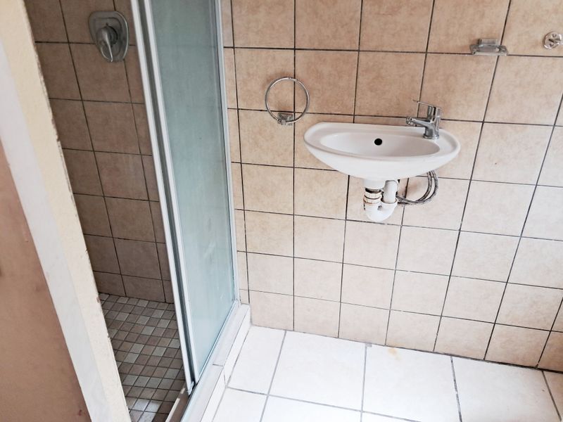 A compact bathroom featuring a shower enclosure and a wall-mounted basin with tiled finishes, currently in need of cosmetic updates.