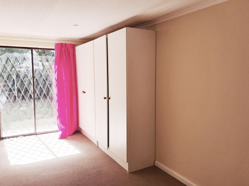 Bedroom featuring built-in cupboards, carpeted flooring, and a sliding glass door with security gate providing access to the exterior.