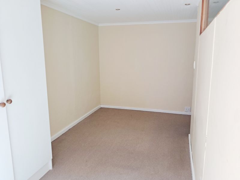 An empty, neutral-toned bedroom featuring built-in cupboards, recessed ceiling lighting, and carpeted flooring.