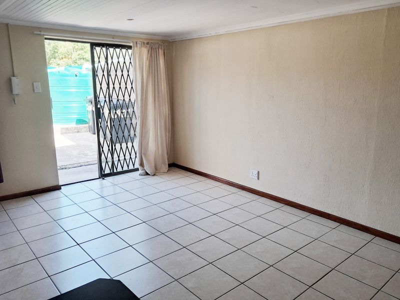 An empty living room featuring tiled flooring, a tongue and groove ceiling, and a sliding glass door with a security gate leading outdoors.