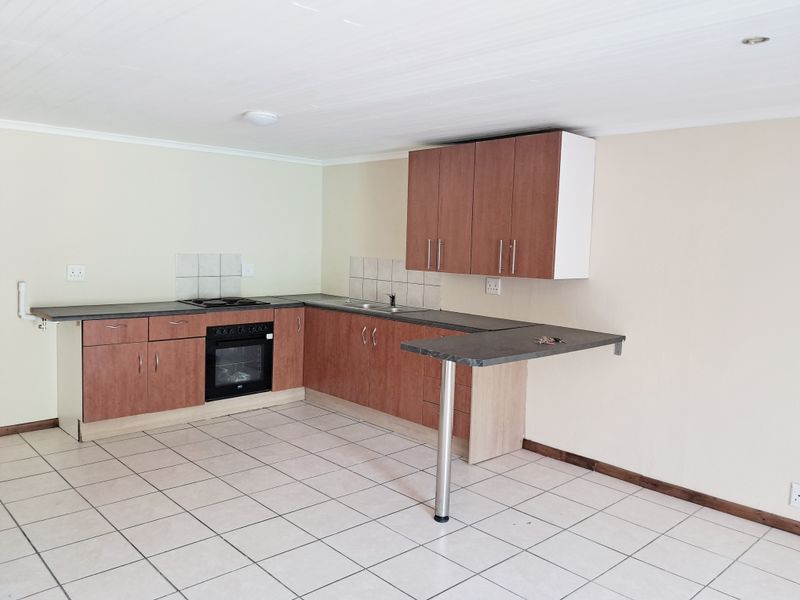 A functional, empty kitchen featuring wood-finish cabinetry, dark laminate countertops, a built-in oven with hob, and tiled flooring with an integrated breakfast bar.