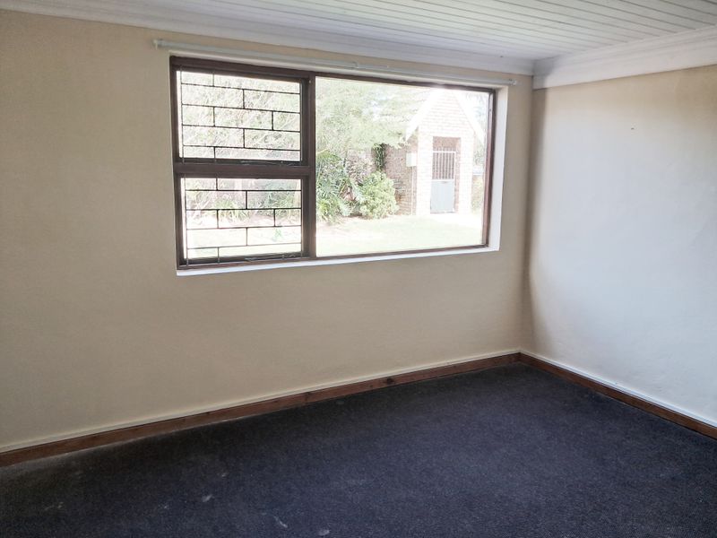An empty bedroom featuring dark carpeting, timber skirting boards, a tongue and groove ceiling, and a window fitted with security bars.