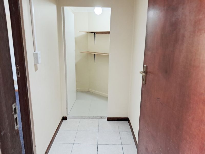 A small, empty utility or storage space featuring tiled flooring and built-in wall shelving, accessible via an internal doorway.