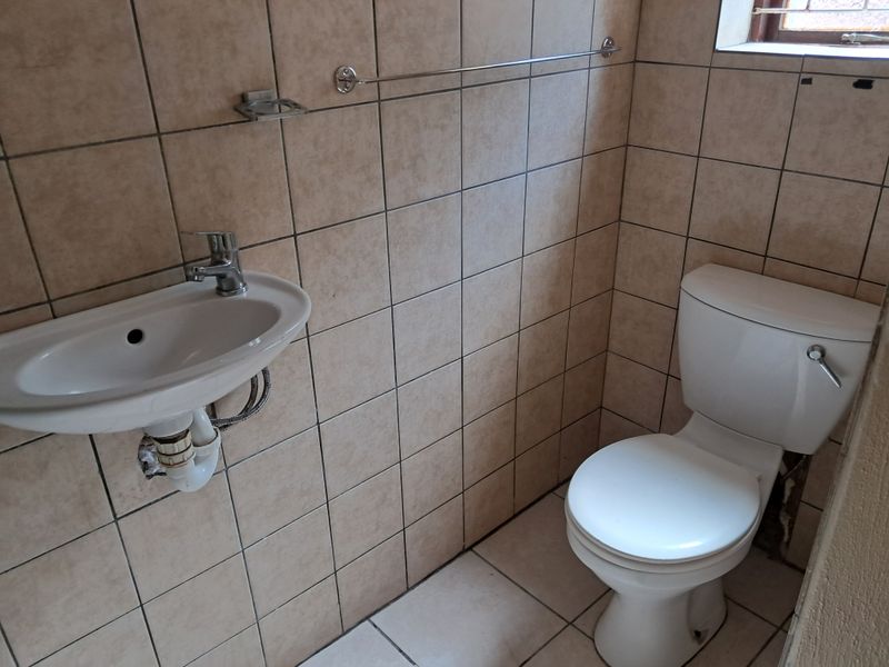 A compact bathroom featuring tiled walls and flooring, equipped with a wall-mounted basin and a standard toilet.