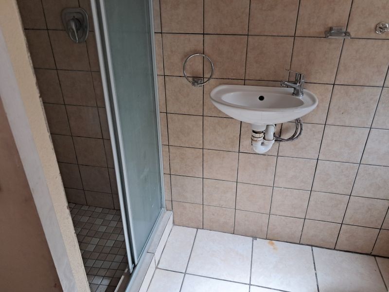 A compact bathroom featuring a shower enclosure and a wall-mounted basin with exposed plumbing, finished with neutral ceramic tiling.