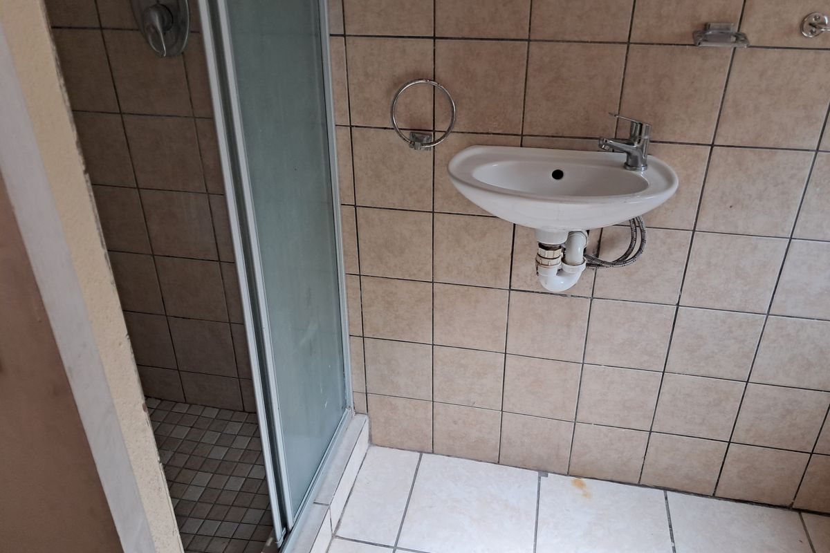A compact bathroom featuring a shower enclosure and a wall-mounted basin with exposed plumbing, finished with neutral ceramic tiling.