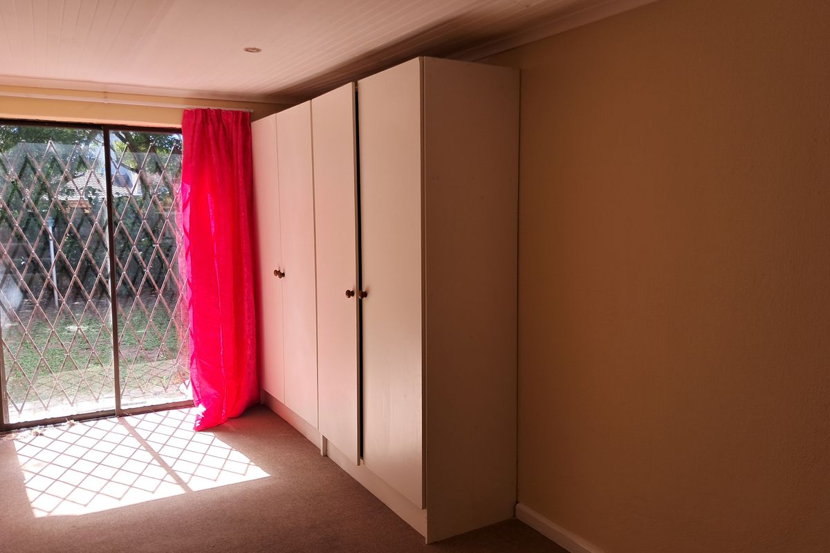 A bedroom featuring built-in cupboards, carpeted flooring, and a sliding glass door with a security gate leading to the exterior.