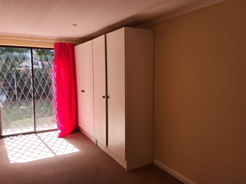 A bedroom featuring built-in cupboards, carpeted flooring, and a sliding glass door with a security gate leading to the exterior.