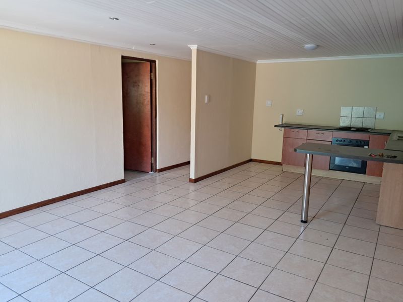An open-plan living and kitchen area featuring tiled flooring, built-in cabinetry, and a breakfast counter, offering a blank canvas for interior design.