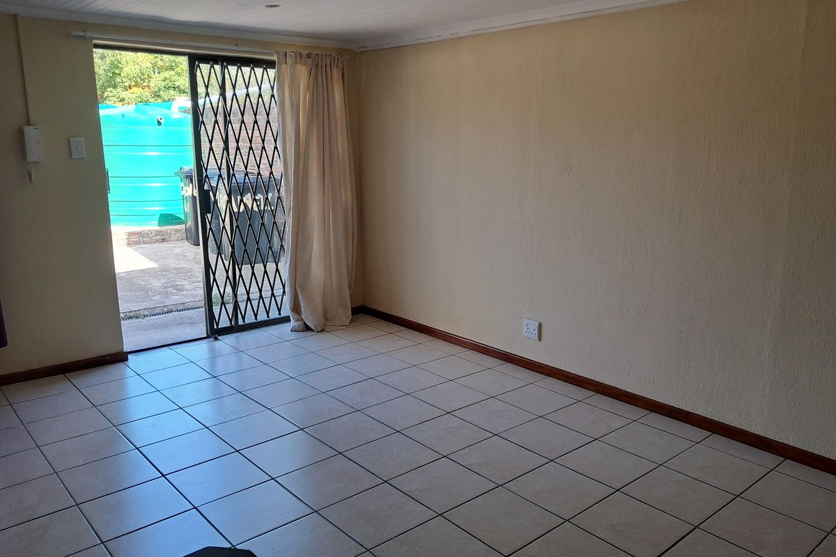 An empty living room featuring tiled flooring, a sliding glass door with a security gate, and direct access to an outdoor area.