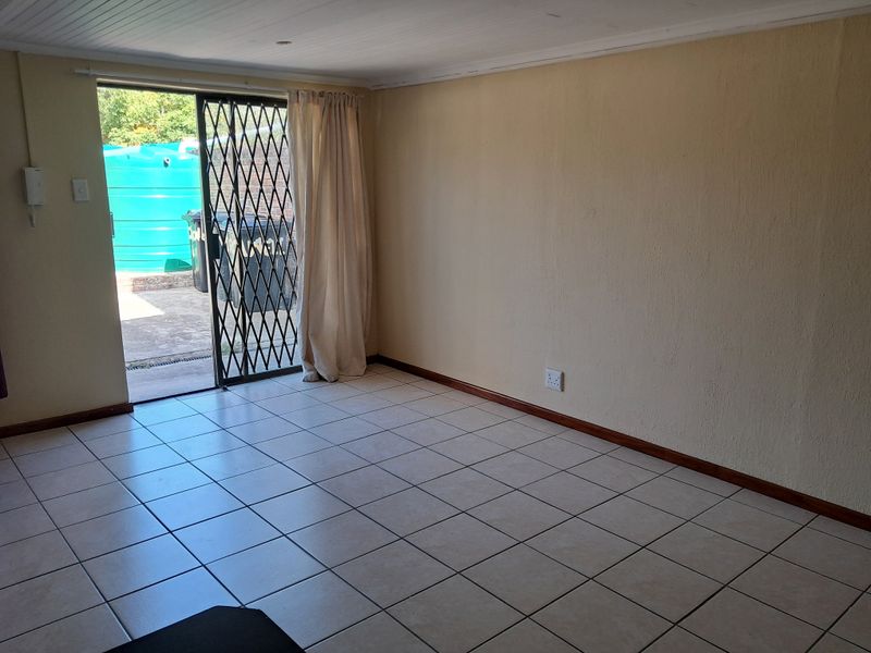 An empty living room featuring tiled flooring, a sliding glass door with a security gate, and direct access to an outdoor area.
