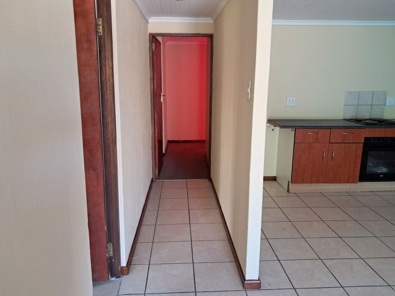 A functional hallway leading to an adjacent kitchen area featuring tiled flooring, wooden door frames, and built-in kitchen cabinetry with an integrated oven.