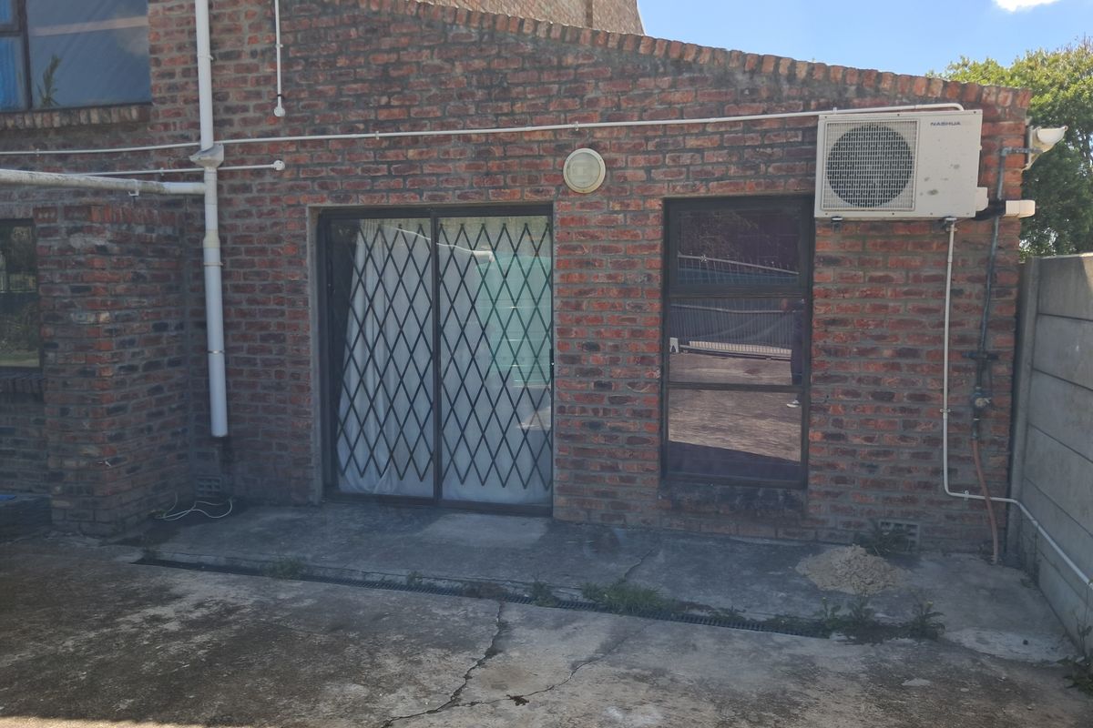 Rear exterior view of the apartment featuring exposed brickwork, a sliding door with security gate, and a concrete patio area.