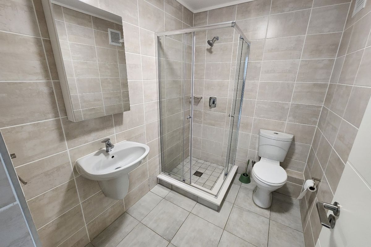 A clean, modern bathroom featuring a glass shower enclosure, wall-mounted basin, and toilet with neutral ceramic tiling throughout.