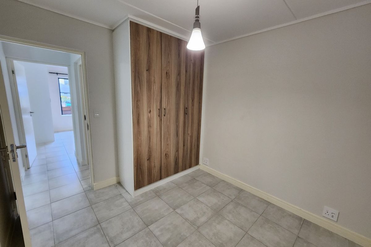 A clean, empty bedroom featuring modern wood-finish built-in wardrobes, neutral tiled flooring, and a simple pendant light fixture.