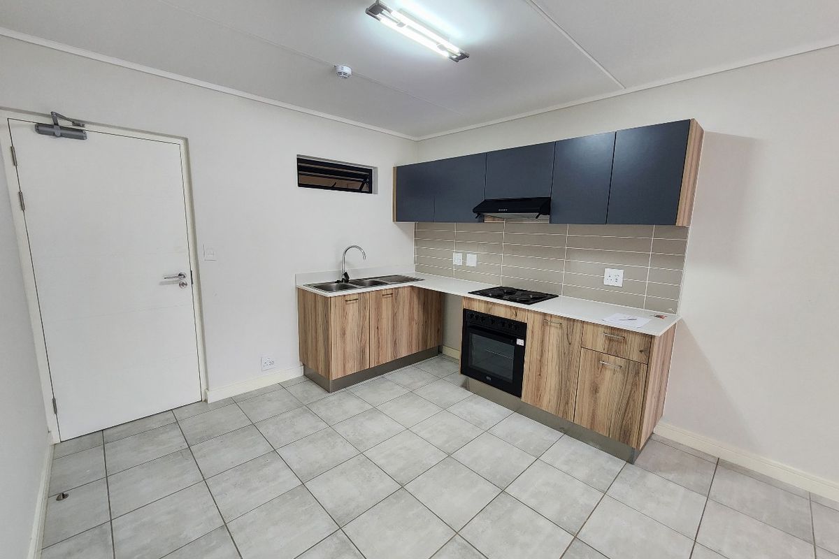Modern kitchen featuring wood-look cabinetry, dark upper cupboards, built-in oven with gas hob, extractor fan, and neutral tiled flooring.
