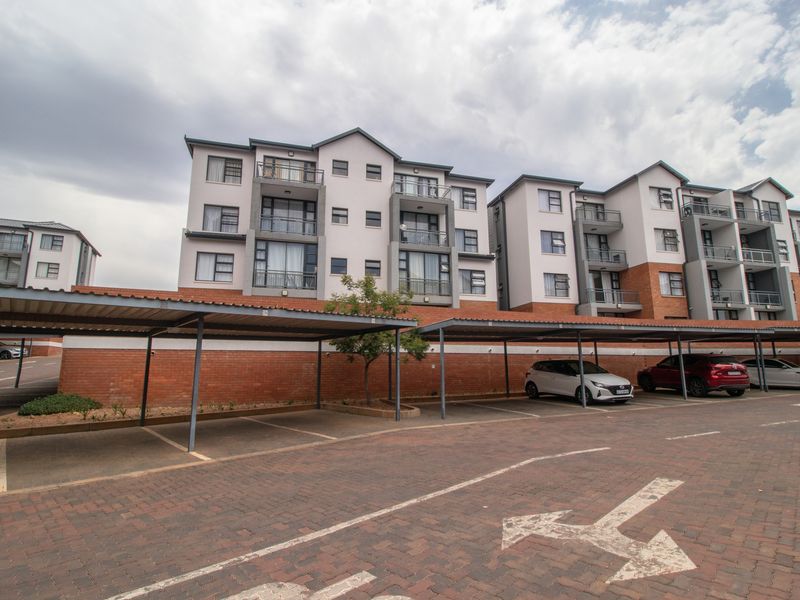Exterior view of a multi-story apartment complex featuring covered parking bays and brick-paved driveway areas.
